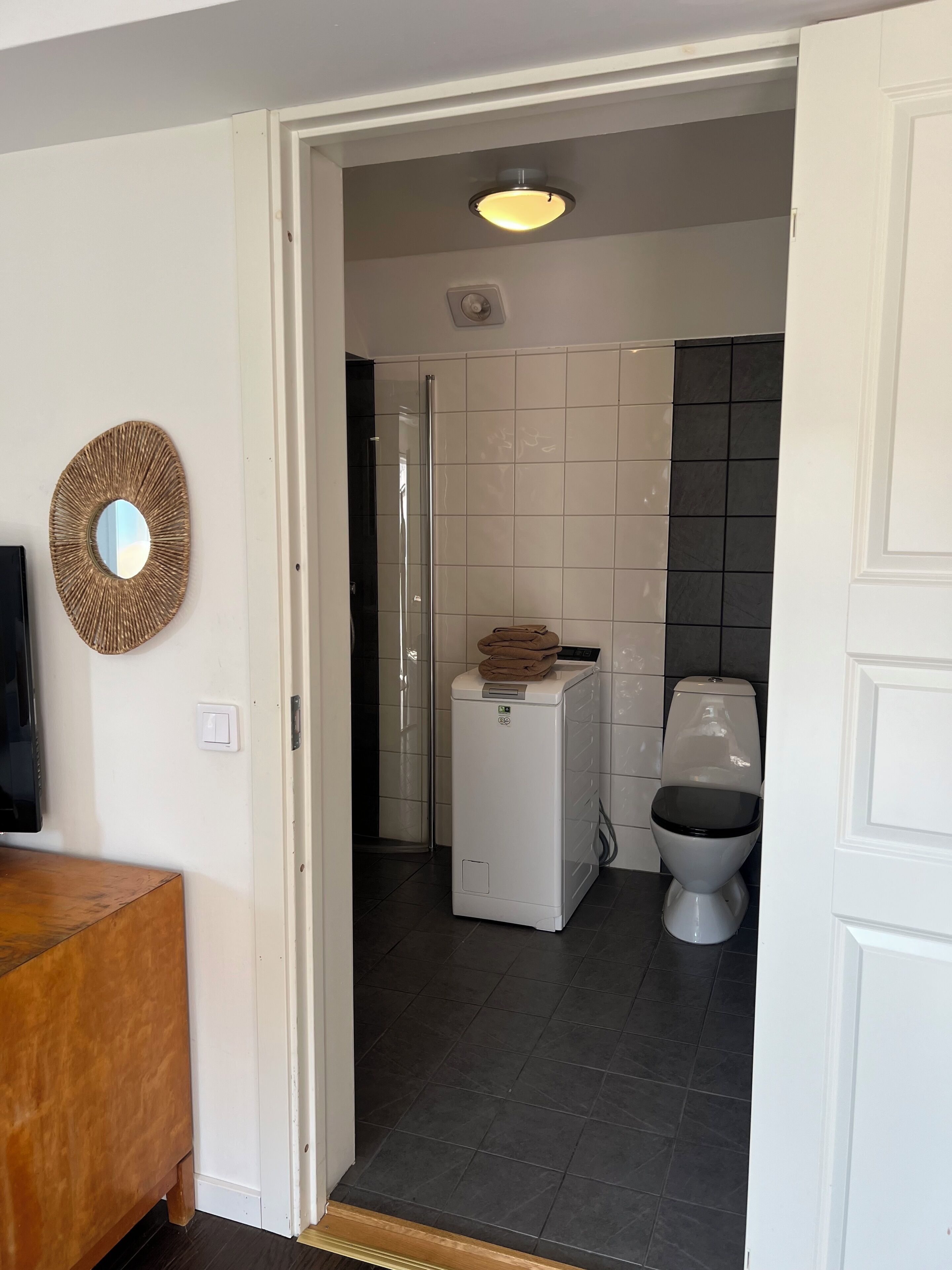 Une salle de bain moderne avec des toilettes blanches, un lave-linge et une douche.