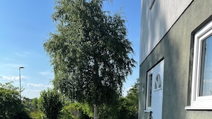 Un espace extérieur aménagé avec des tables et des bancs en bois, un sol en gravier et un bâtiment doté d’une fenêtre et d’une porte.