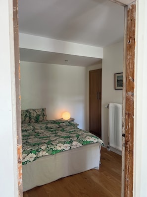 A bedroom with a bed, a bedside lamp, a radiator, and a wooden wardrobe. - Sjöbacken – Lovely apartment in the heart of Braås (Braås)