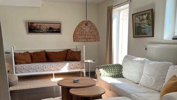 Un salon moderne avec un canapé, un pouf et une table basse ronde en bois. Un luminaire suspendu se trouve au-dessus de la table basse.