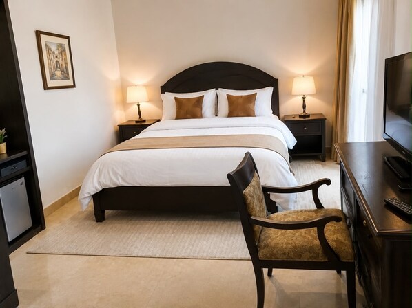 A hotel room with a bed, two bedside tables with lamps, a television, a desk with a chair, and a small potted plant. - Double Room in a Luxury Villa (New Cairo)