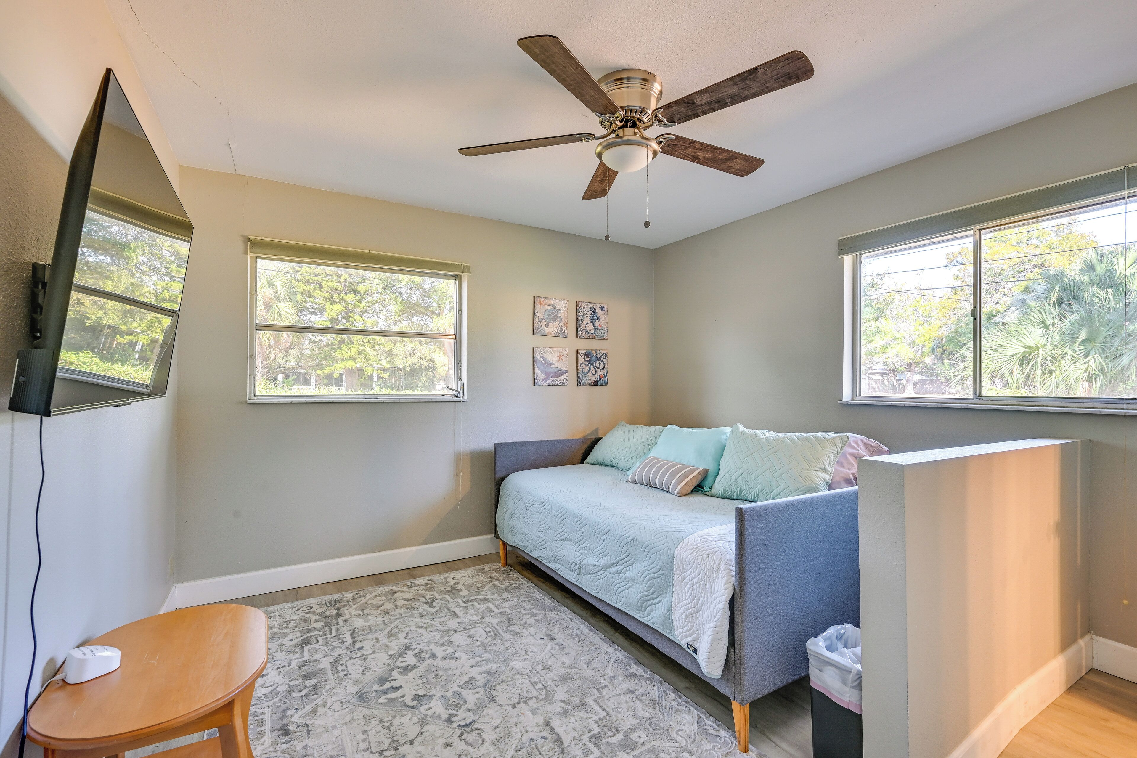 A bedroom with a bed, a ceiling fan, a window, and a small table.