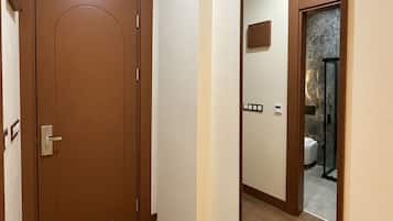 A hallway with a wooden door and a large mirror reflecting a bathroom with a shower and toilet.