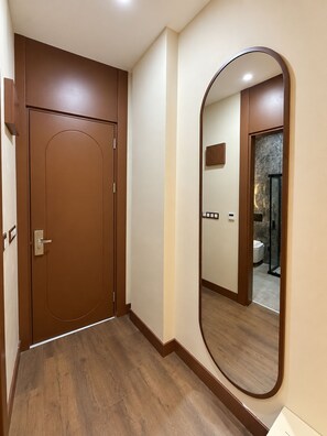 Un pasillo con una puerta de madera y un espejo grande que refleja un baño con ducha e inodoro.