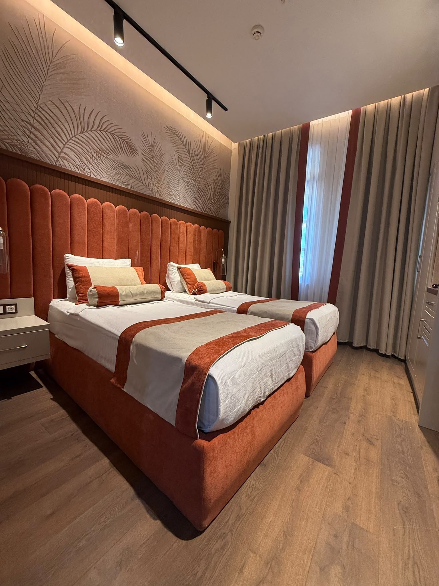 A double bed with a wooden headboard, two bedside tables, and a large window with curtains.