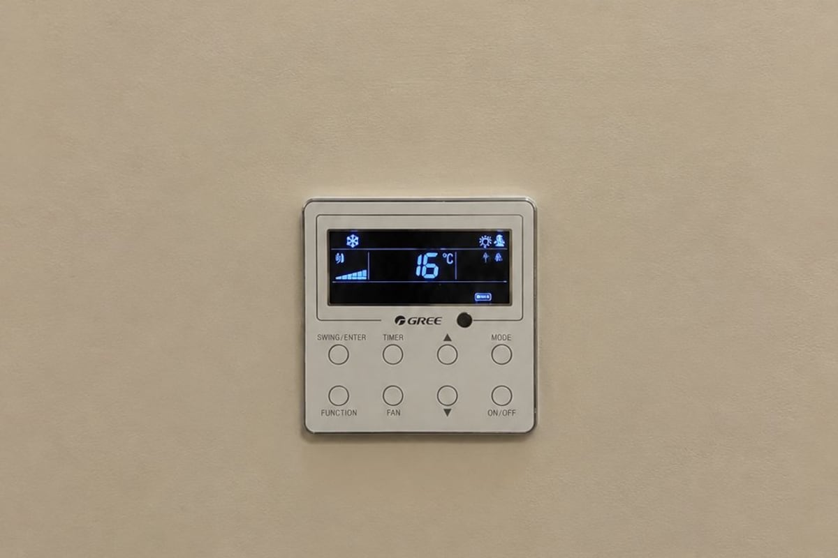 A wall-mounted thermostat with a digital display, control buttons, and a brand name.
