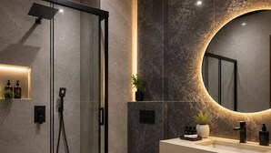 Ein modernes Badezimmer mit einer Duschkabine, einer weißen Toilette und einem Waschtisch mit Spiegel.