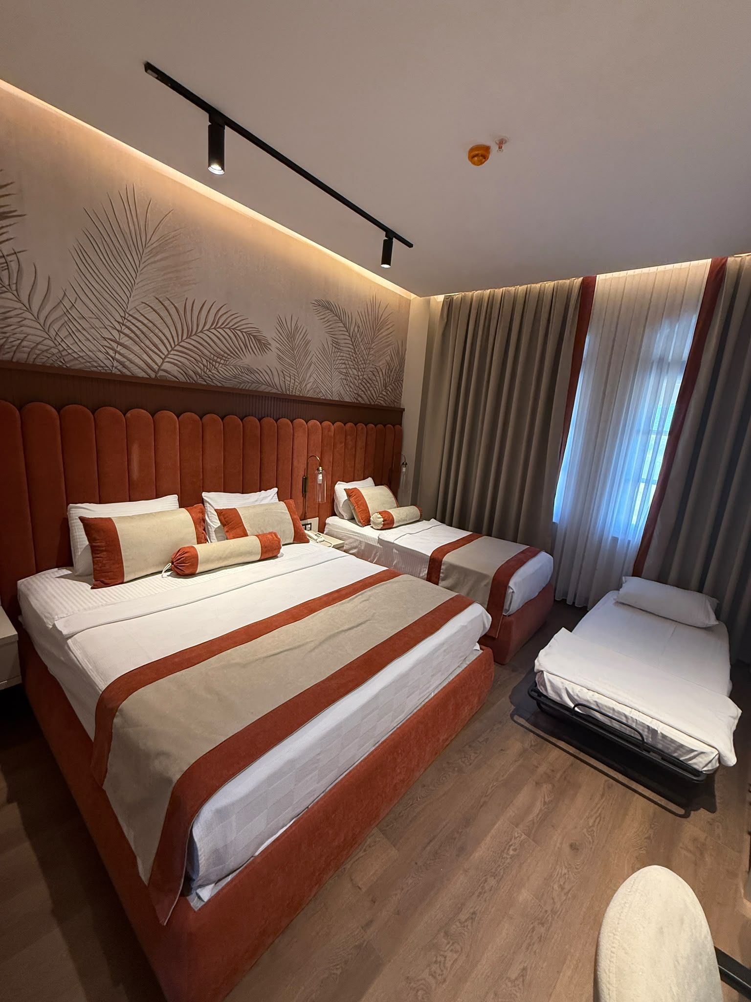 A hotel room with a large bed, two smaller beds, a desk, and a chair.