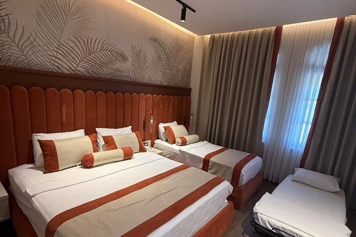 A hotel room with a large bed, two smaller beds, a desk, and a chair.