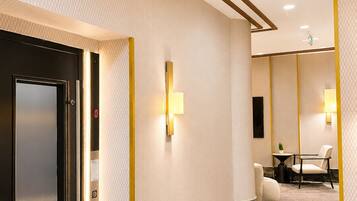 A modern hotel corridor with a marble floor, recessed ceiling lights, and a black elevator door.