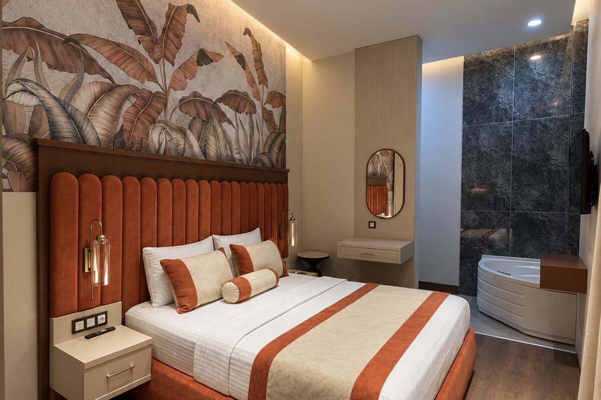 A modern bedroom with a large bed, a nightstand, a mirror, a vanity, and a bathroom with a bathtub.