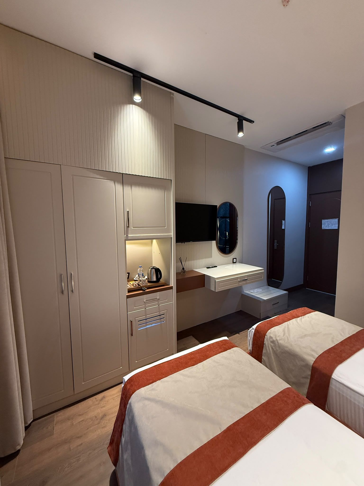Quarto de hotel com guarda-roupa, penteadeira com espelho, cama e porta.