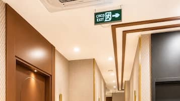 A hotel corridor with a green exit sign, a blue trash bin, and a door labeled '210'.