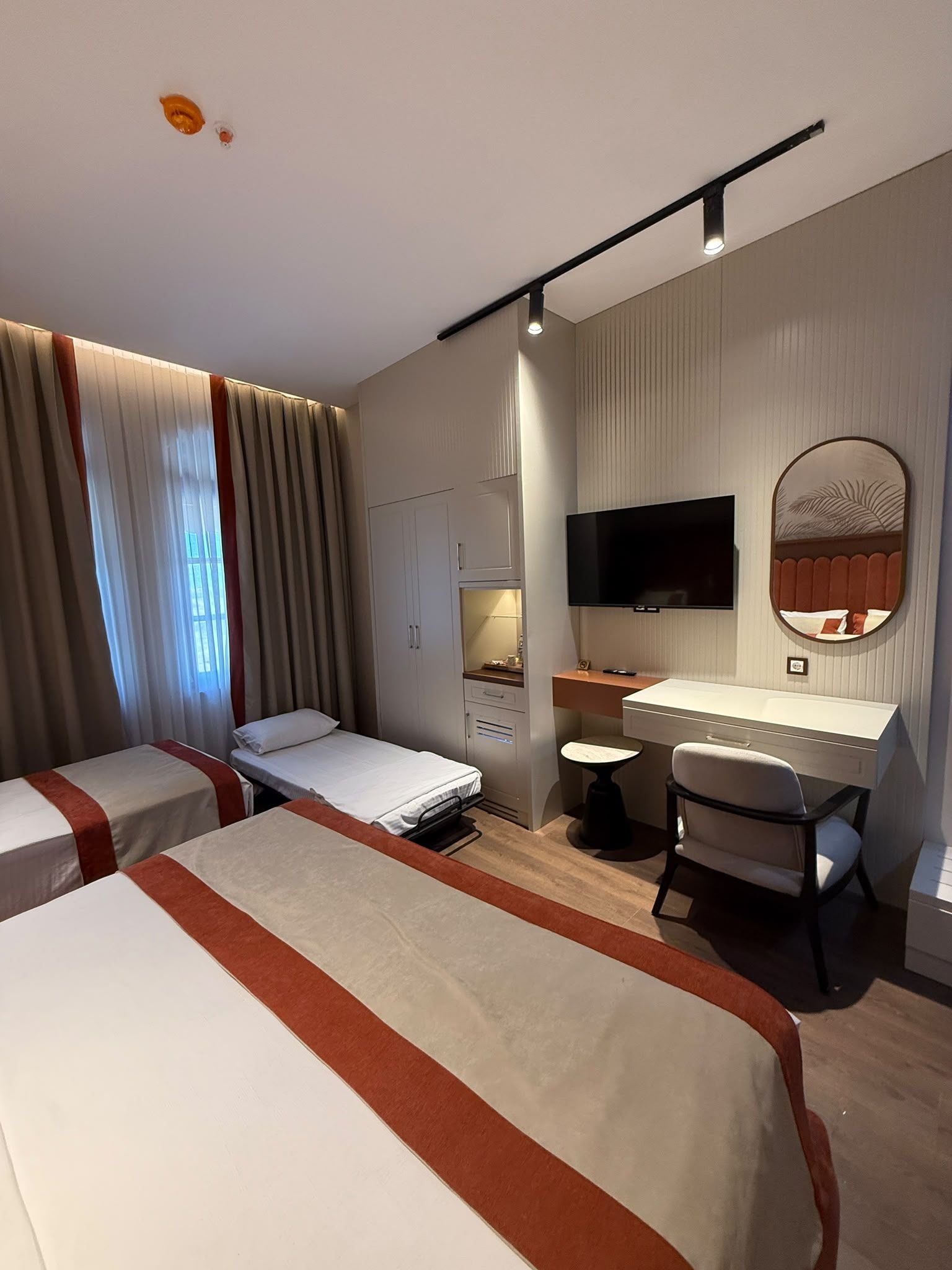A hotel room with two beds, a desk, a chair, a television, and a mirror.