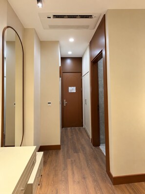 A hotel hallway with wooden flooring, a door with a sign, and a mirror on the left. - Ahura Otel (Diyarbakir)