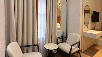 A hotel room with two armchairs, a small round table, a mirror, a television, and a bedside table.