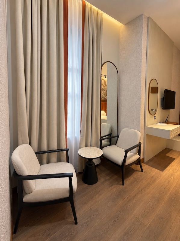 A hotel room with two armchairs, a small round table, a mirror, a television, and a bedside table.