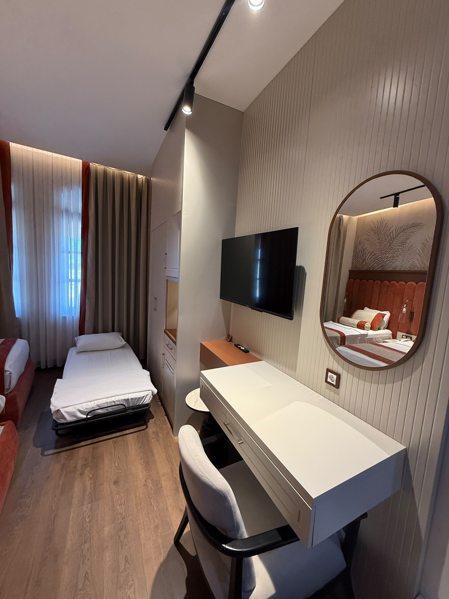 Una habitación de hotel con cama, escritorio, silla, televisor y espejo.