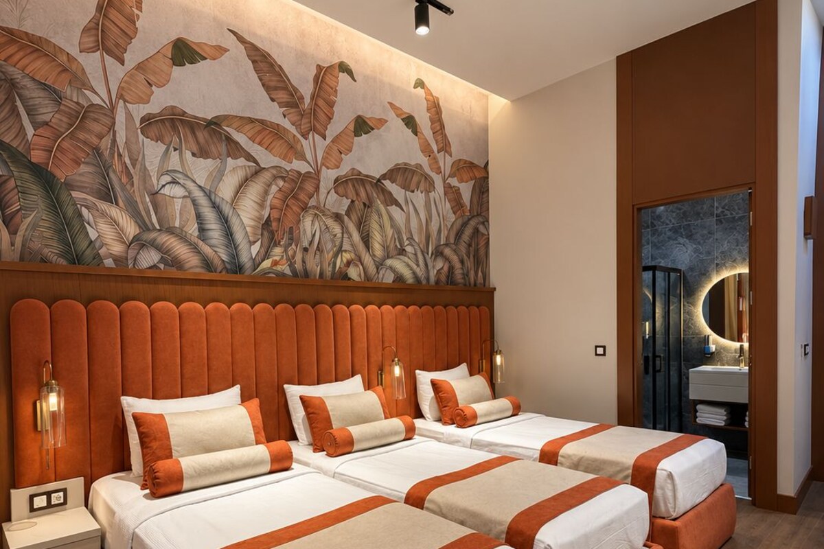 A hotel room with a large bed, a nightstand, a wall mural, and a bathroom with a mirror.