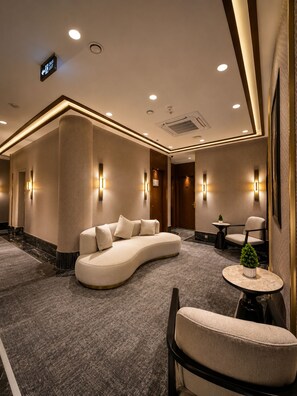 Un hall de hotel con un sofá curvo, una mesa redonda con una planta y una silla.