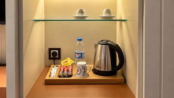 Un minibar con repisa de vidrio, dos tazas, una botella de agua, una tetera y algunos bocadillos.