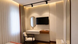 A hotel room with a bed, a desk with a chair, a television, and a mirror.