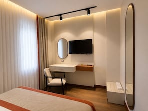 A hotel room with a bed, a desk with a chair, a television, and a mirror.