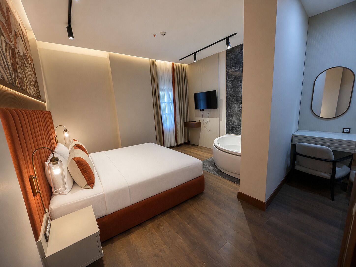 A modern hotel room with a large bed, a bathroom with a bathtub, a vanity with a mirror, and a flat-screen TV mounted on the wall.