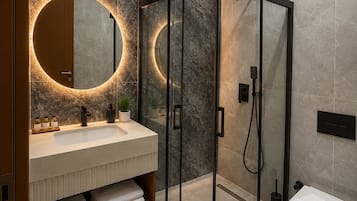 Ein modernes Badezimmer mit einer gläsernen Duschkabine, einem runden Spiegel mit Beleuchtung und einem weißen Waschbecken.
