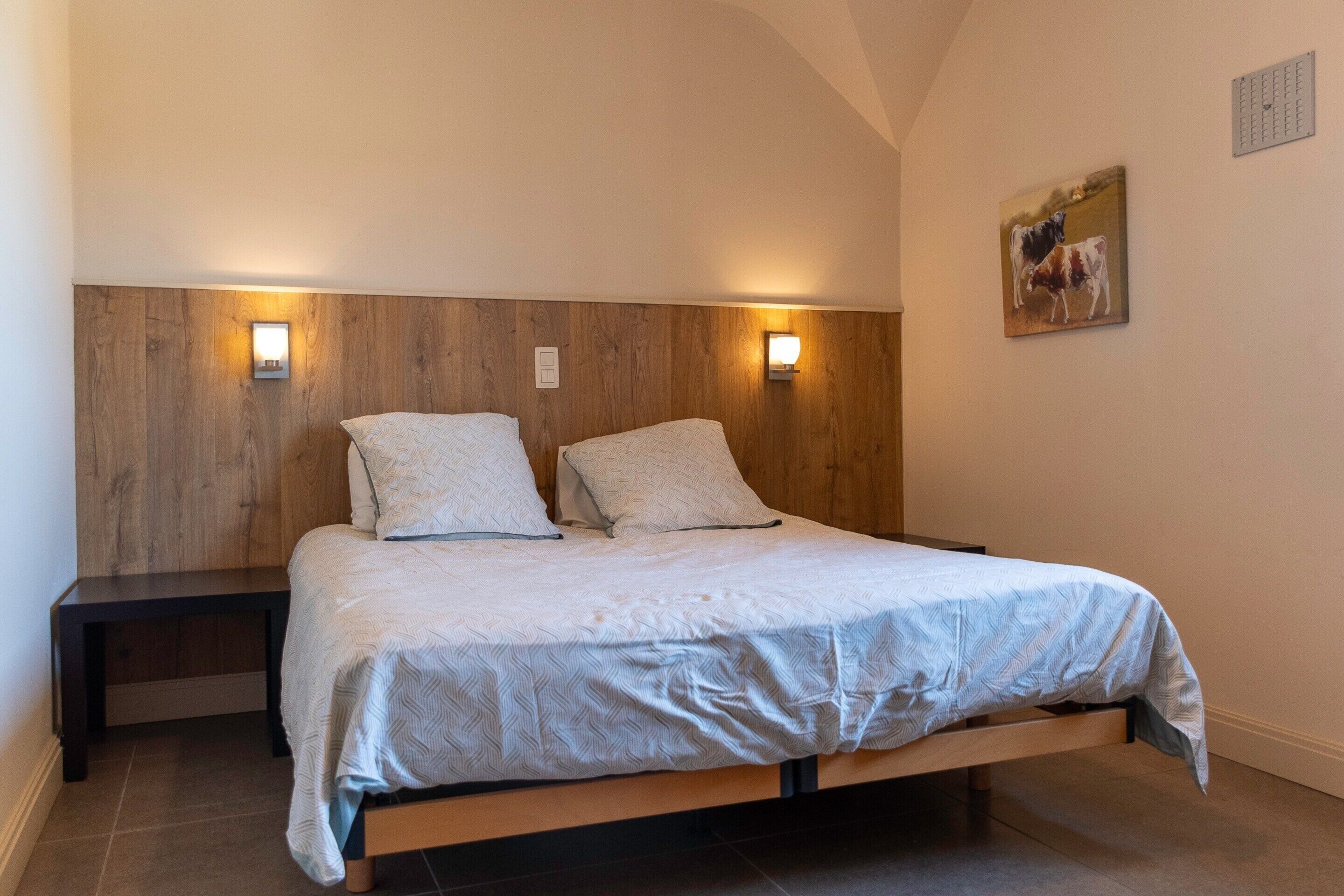 Ein Schlafzimmer mit einem hölzernen Kopfende, zwei Nachttischen, einem Bett mit gemustertem Bettbezug und einer Wandleuchte.