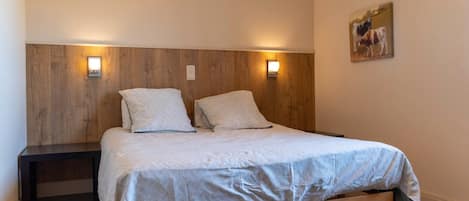 Ein Schlafzimmer mit einem hölzernen Kopfende, zwei Nachttischen, einem Bett mit gemustertem Bettbezug und einer Wandleuchte.