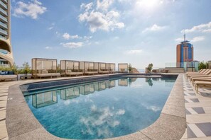A swimming pool with lounge chairs and sunbeds, surrounded by a high-rise building and clear skies. - Official Mercury Suites: Designer 1BR w/Balcony (St. Julian`s)