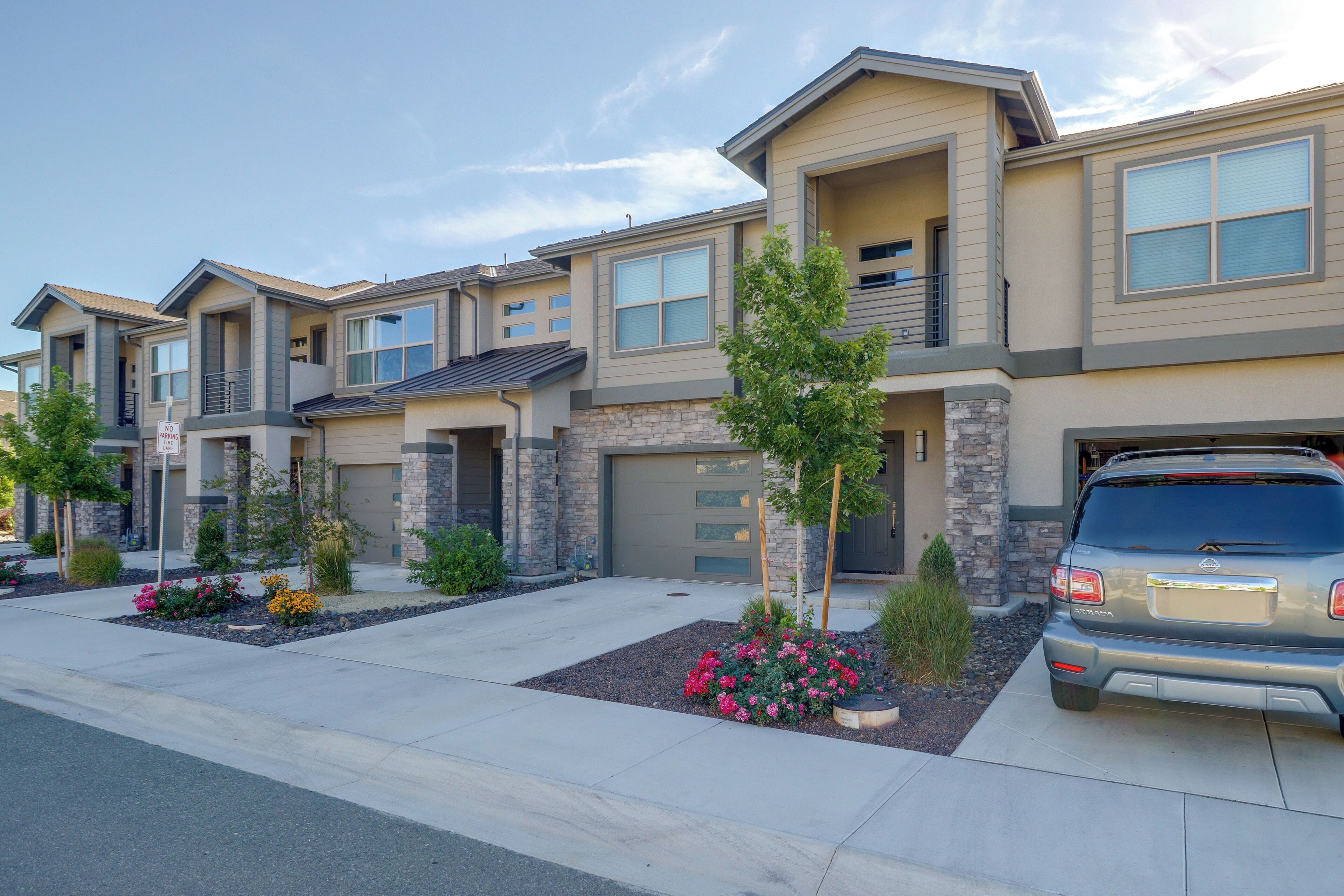 A row of modern two-story townhouses with attached garages, landscaped front yards, and a clear sky.