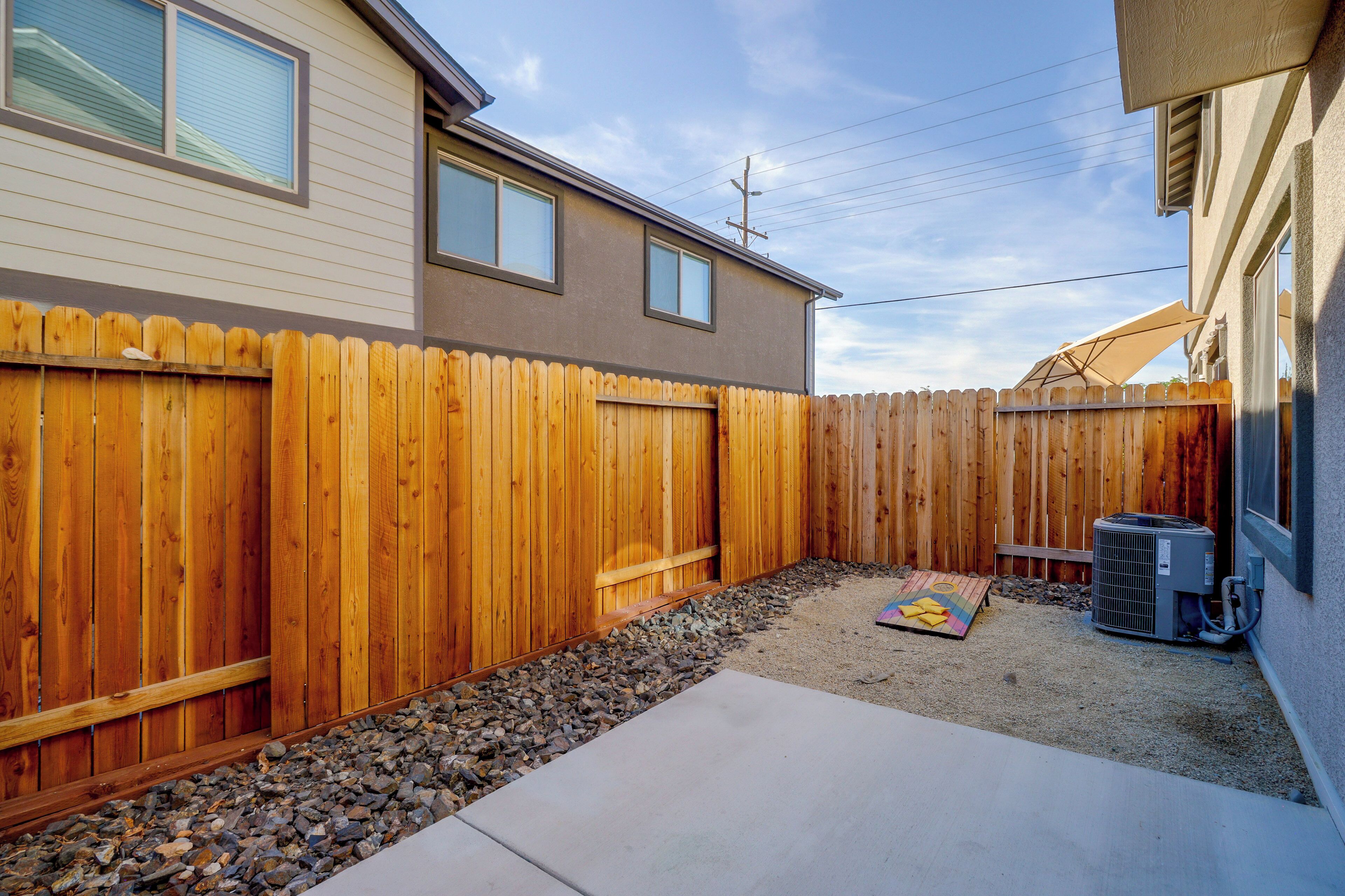 A backyard with a wooden fence, a concrete patio, and an air conditioning unit.
