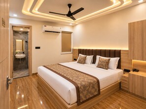 A modern bedroom with a large bed, bedside tables, a ceiling fan, and an air conditioning unit. - Hotel Akrati Inn Vrindavan (Mathura)