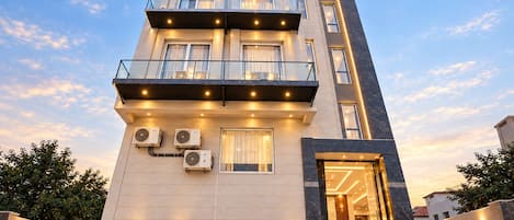 Un hotel de varios pisos con diseño moderno, que cuenta con balcones, unidades de aire acondicionado y una entrada bien iluminada.