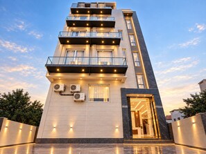 A multi-story hotel with a modern design, featuring balconies, air conditioning units, and a well-lit entrance. - Hotel Akrati Inn Vrindavan (Mathura)