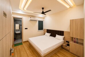 A hotel room with a bed, bedside table, wardrobe, and a ceiling fan. - Hotel Akrati Inn Vrindavan (Mathura)