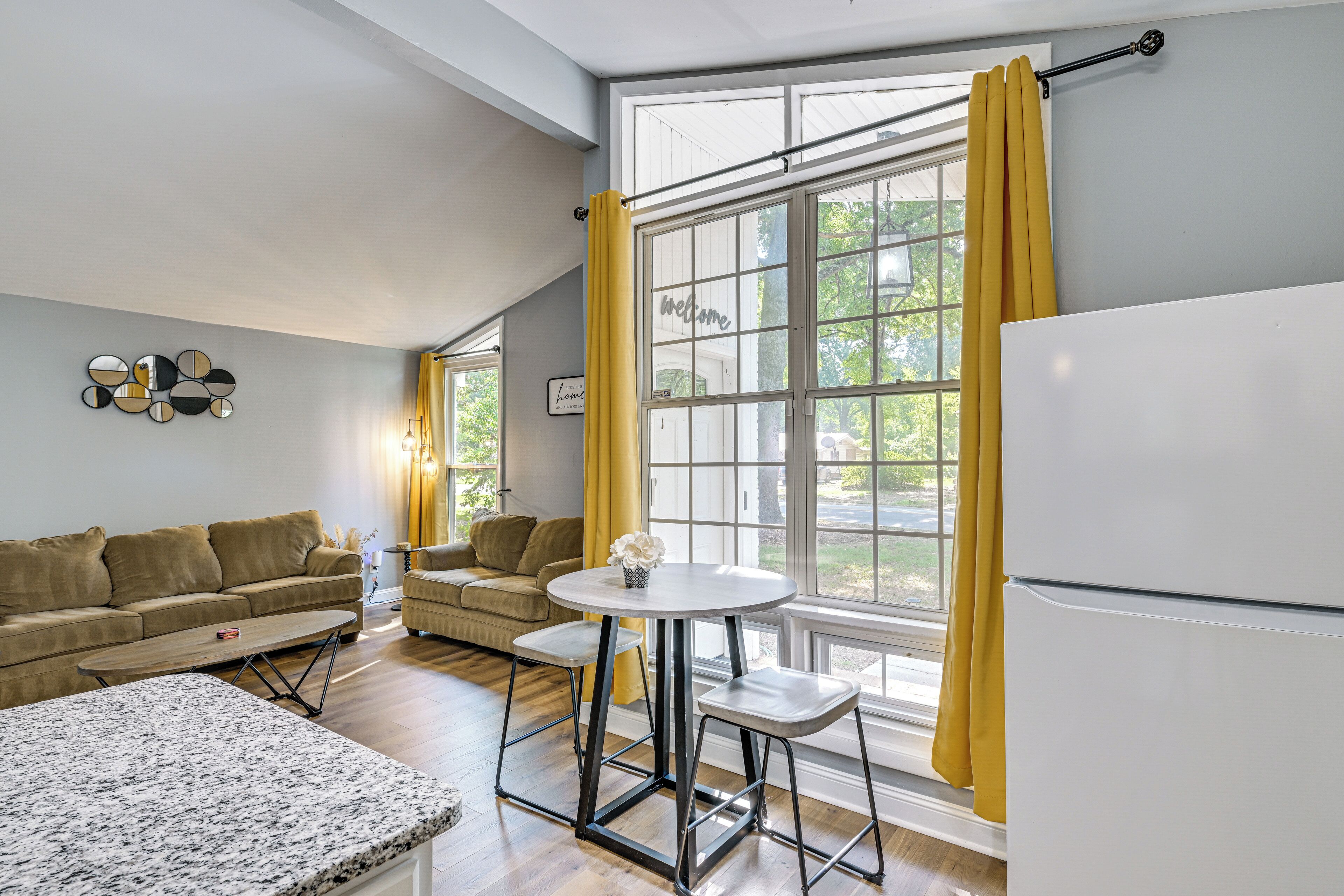 Un espace de vie compact comprenant un canapé, une petite table à manger, un réfrigérateur et une fenêtre avec des rideaux.