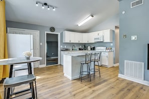 A modern kitchen with white cabinets, a central island with bar stools, a microwave, and a coffee machine. - Centrally Located Charlotte Home w/ Patio & Yard! (Charlotte)
