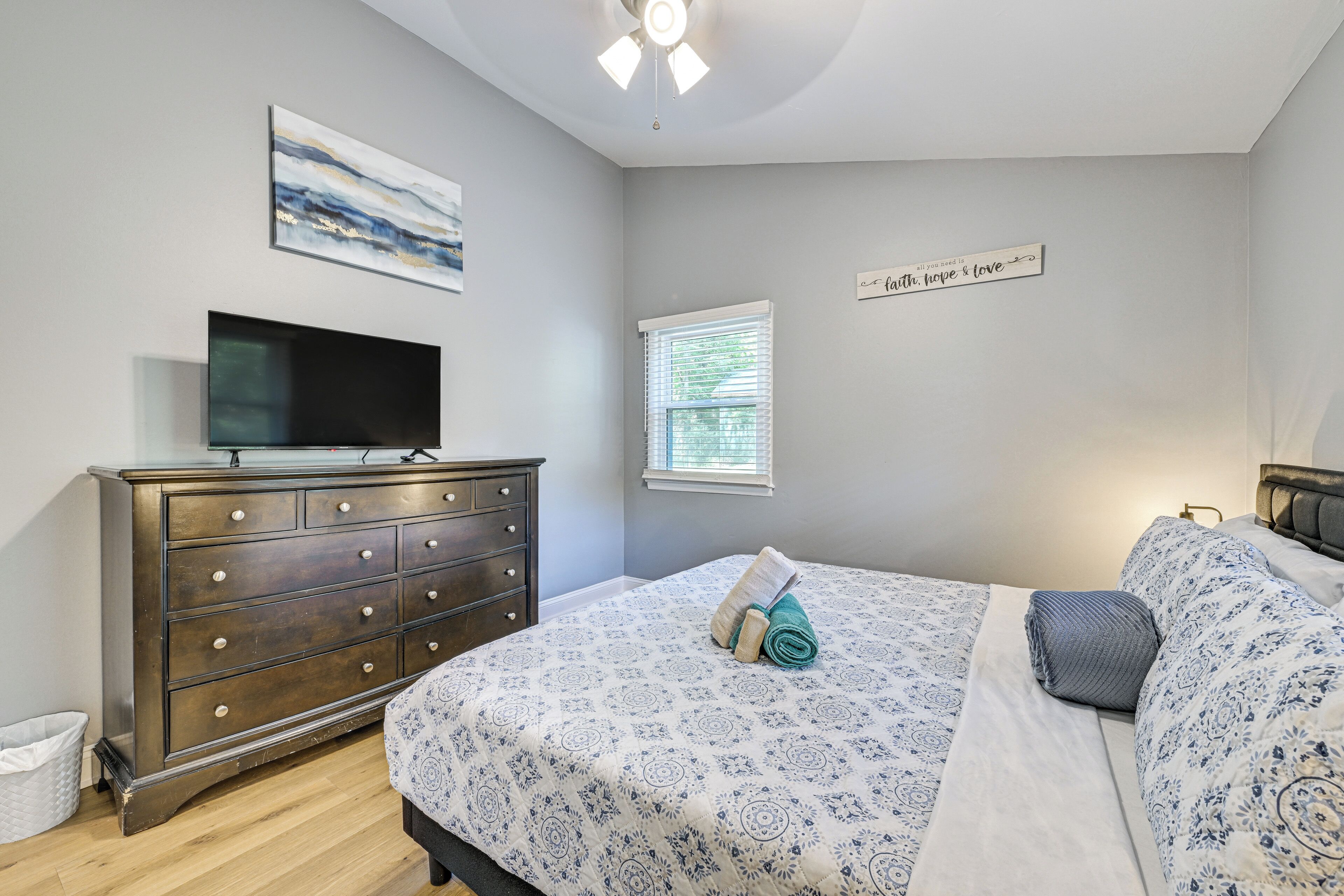A bedroom with a bed, a dresser, a television, a window, and a wall sign.