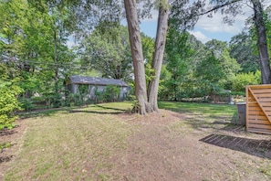 A backyard with a small shed, a wooden bench, and a grassy area surrounded by trees. - Centrally Located Charlotte Home w/ Patio & Yard! (Charlotte)