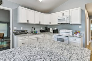 A modern kitchen with white cabinets, a granite countertop, a microwave, a coffee maker, and a stove. - Centrally Located Charlotte Home w/ Patio & Yard! (Charlotte)