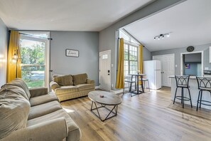 A spacious living area with a sofa, a coffee table, and a kitchen area with a refrigerator and bar stools.