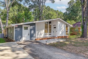 A small, single-story building with a white exterior, a front door, and a garage door. - Centrally Located Charlotte Home w/ Patio & Yard! (Charlotte)