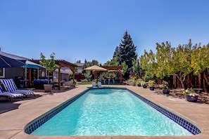 A rectangular swimming pool with a tiled edge, surrounded by lounge chairs and a covered patio area.