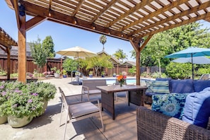 An outdoor patio with a pergola, seating, a pool, and potted plants.