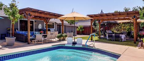 Un patio trasero con piscina, mobiliario de jardín y una pérgola con sombrilla.