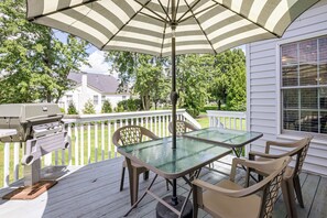 An outdoor patio with a table and chairs, a grill, and a striped umbrella.
