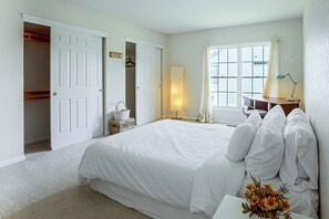 A bedroom with a large bed, a bedside table with a lamp, a window with blinds, and a closet with hanging clothes. - Lake Views & Work Spaces: Quiet Hilliard Home! (Hilliard)